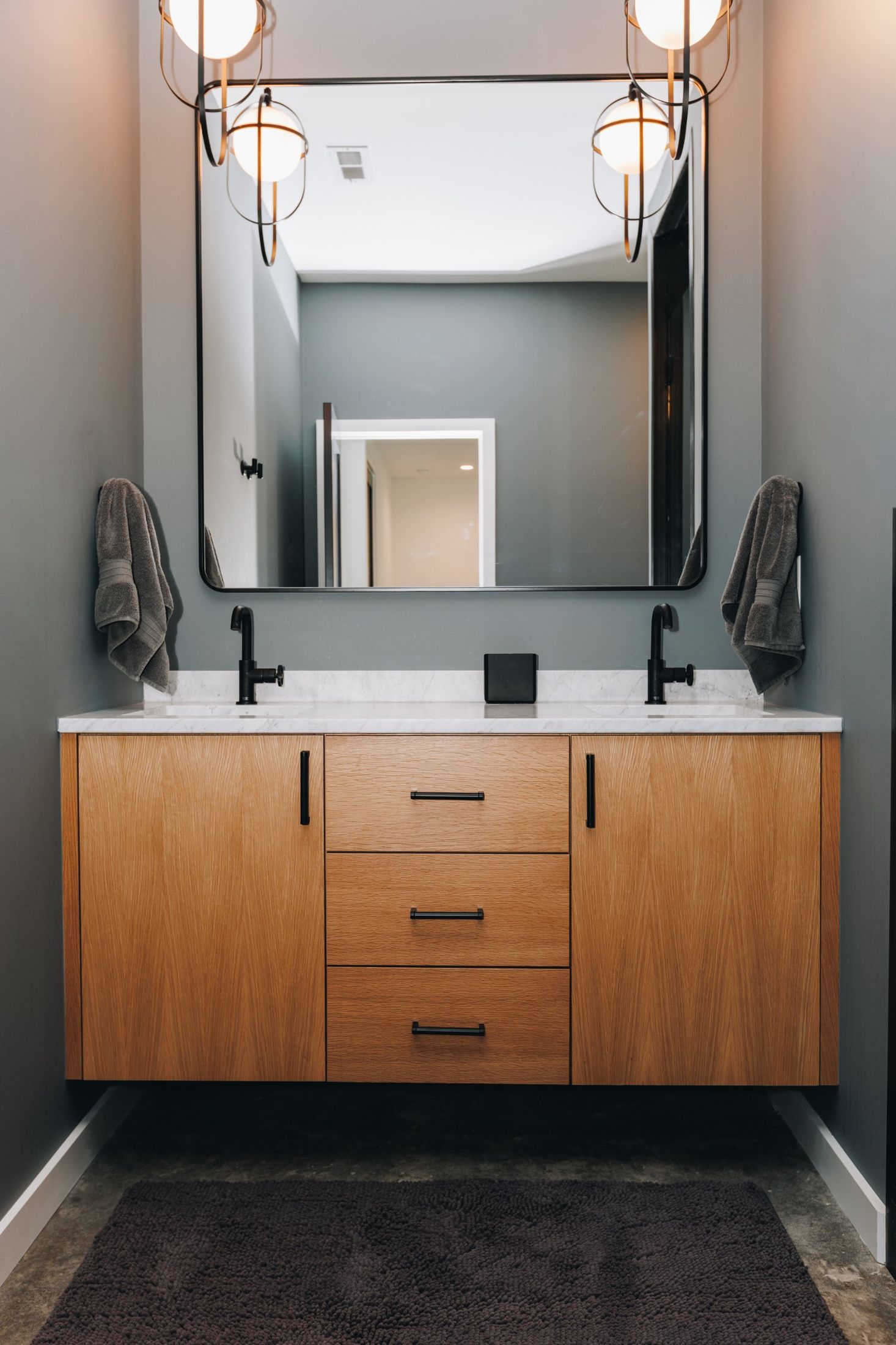 Floating oak double vanity under a black-framed mirror and globe pendants