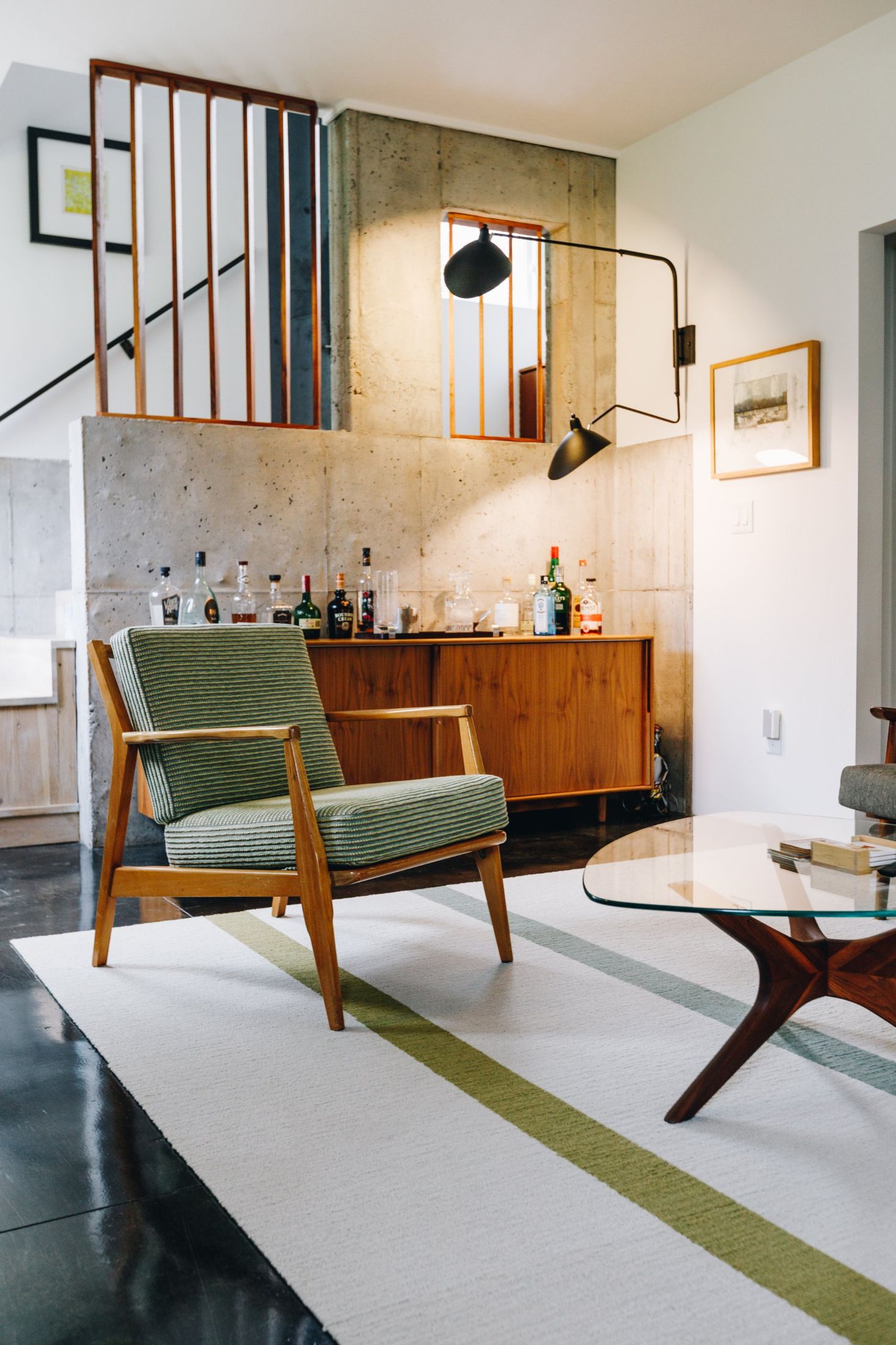 Green mid-century lounge chair in front of a walnut credenza and concrete wall