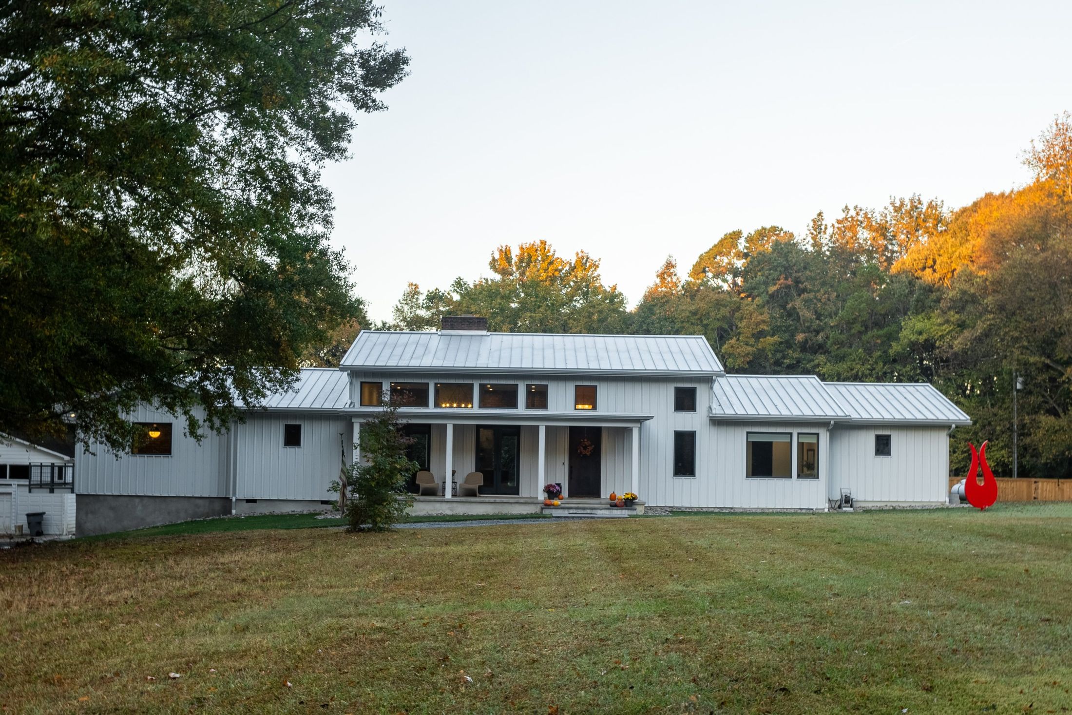 White board-and-batten farmhouse with a standing seam metal roof at dusk