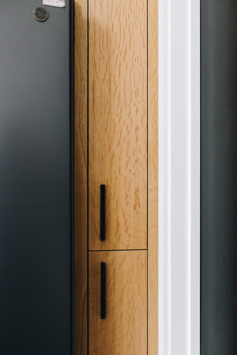 Rift-sawn oak cabinetry with black pulls beside a blackened panel
