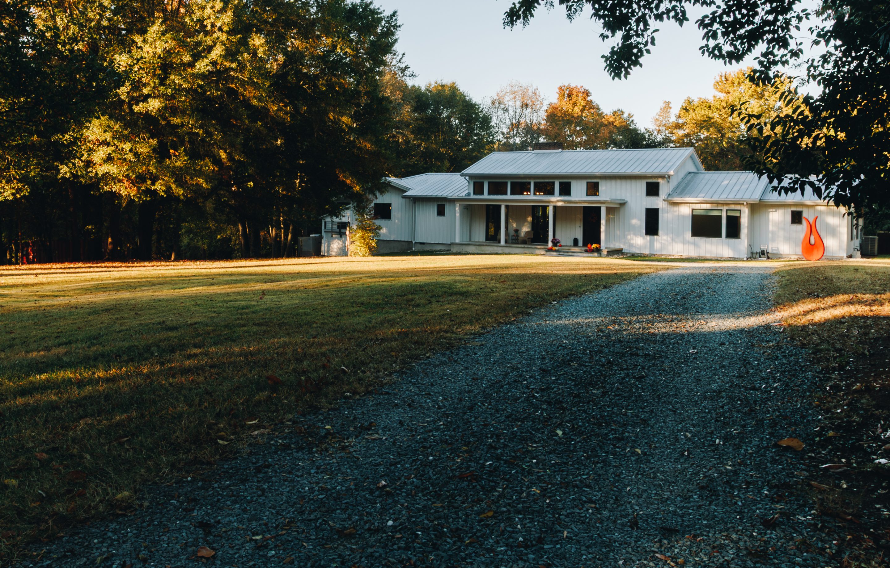 White board-and-batten farmhouse set back at the end of a long gravel drive