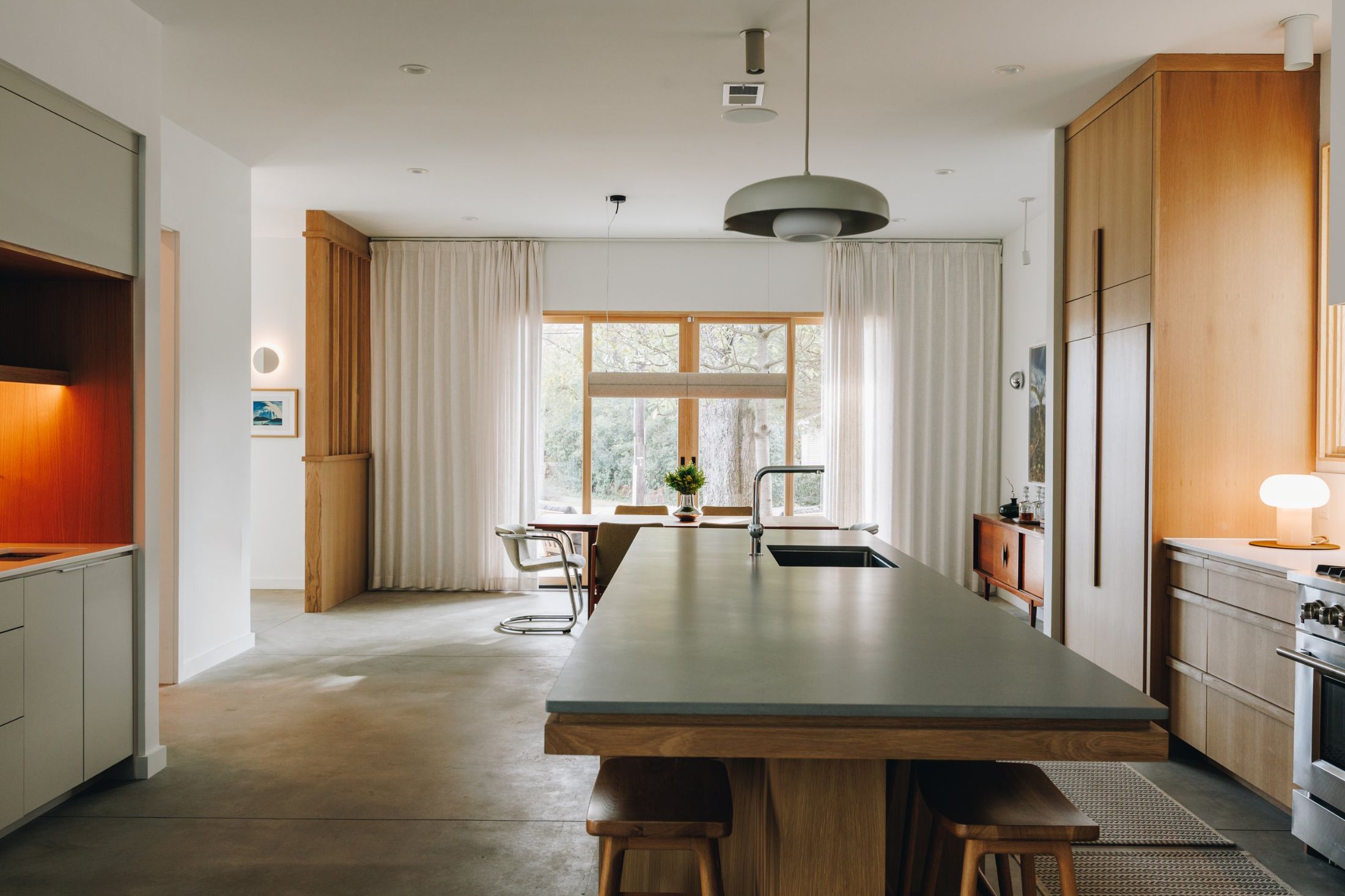 Long concrete-topped oak island leading to a dining area with linen curtains
