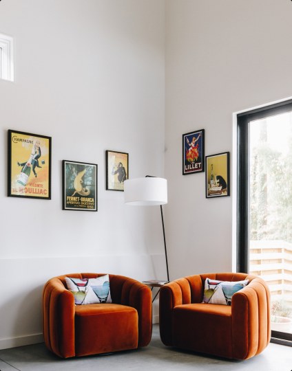 Two rust velvet swivel chairs below vintage posters